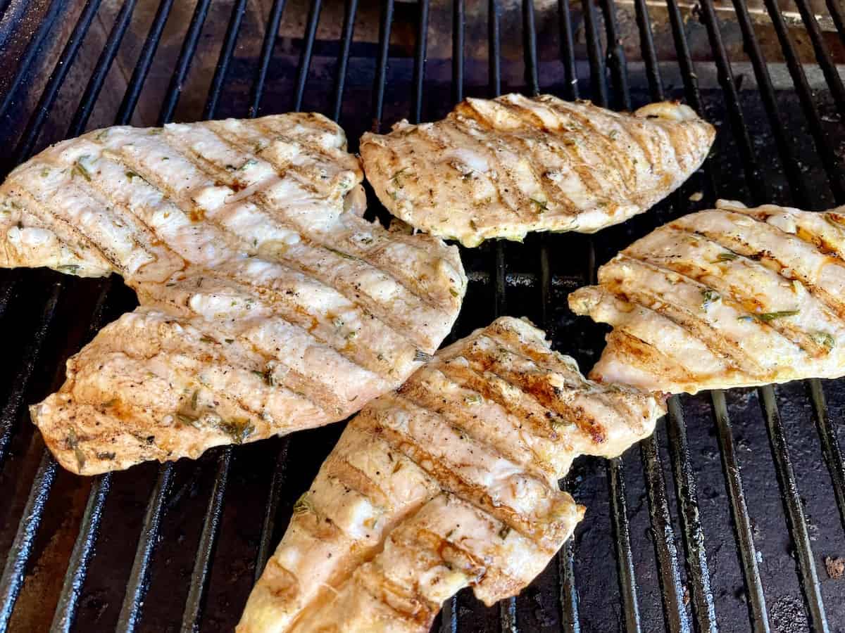 5 chicken breast cutlets cooking on a grill grate with charred grill lines on them