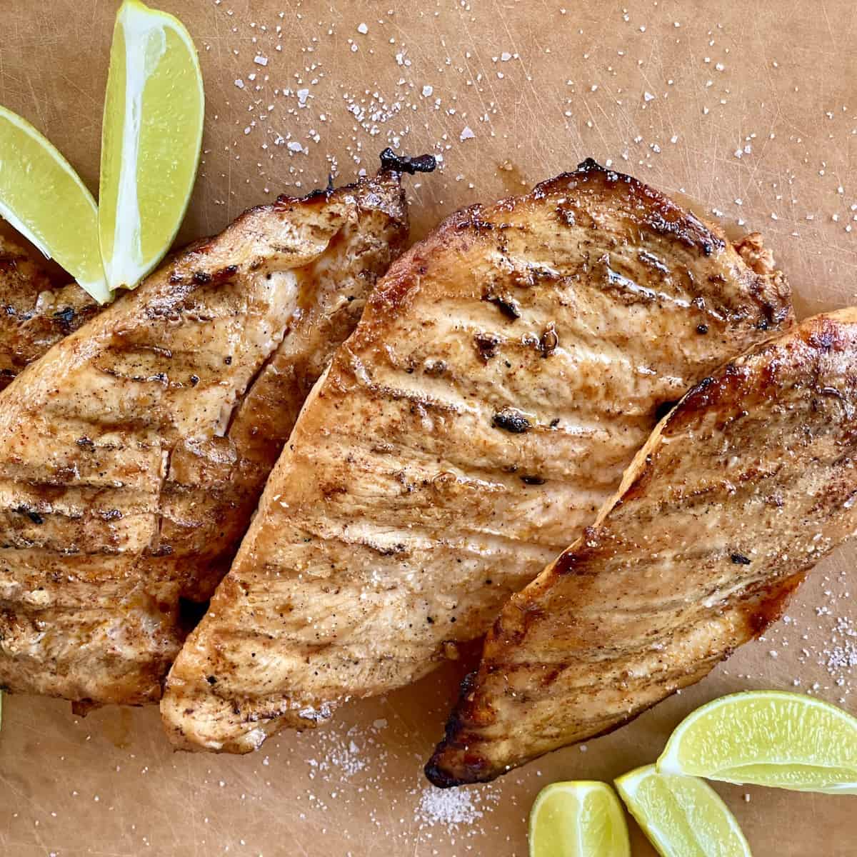 3 grilled pieces of chicken on a cutting board sprinkled with kosher salt and lime slices