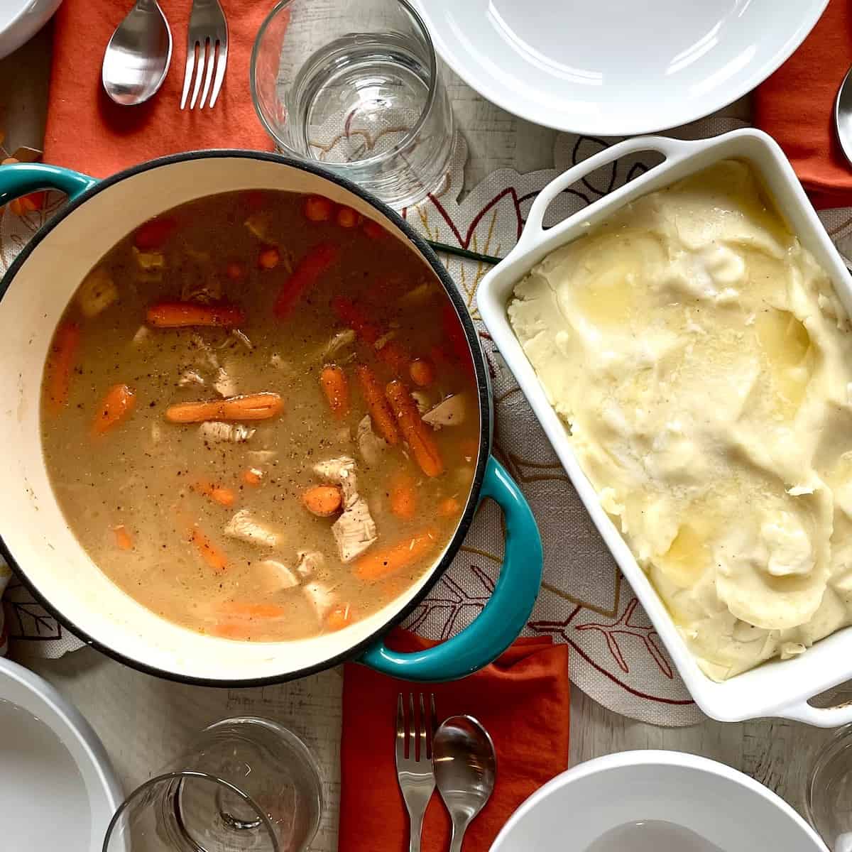 teal cast iron pot filled with rotisserie chicken stew showing chicken pieces and carrots served on a table with mashed potatoes and a table set with orange napkins and flowers