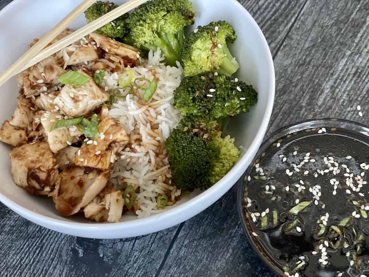 chicken teriyaki bowl with steamed rice chicken breast and fresh broccoli on a grey wood table with more sauce on the side