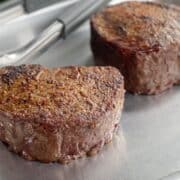 2 7 ounce filets cooked on the traeger grill resting on a small sheet pan with tongs