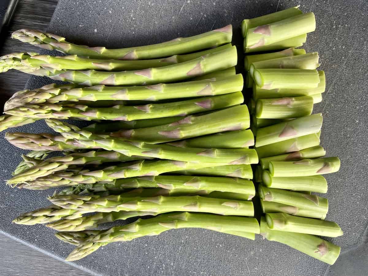 a large pile of asparagus spears lined up on a black cutting board with the bottoms trimmed next to them