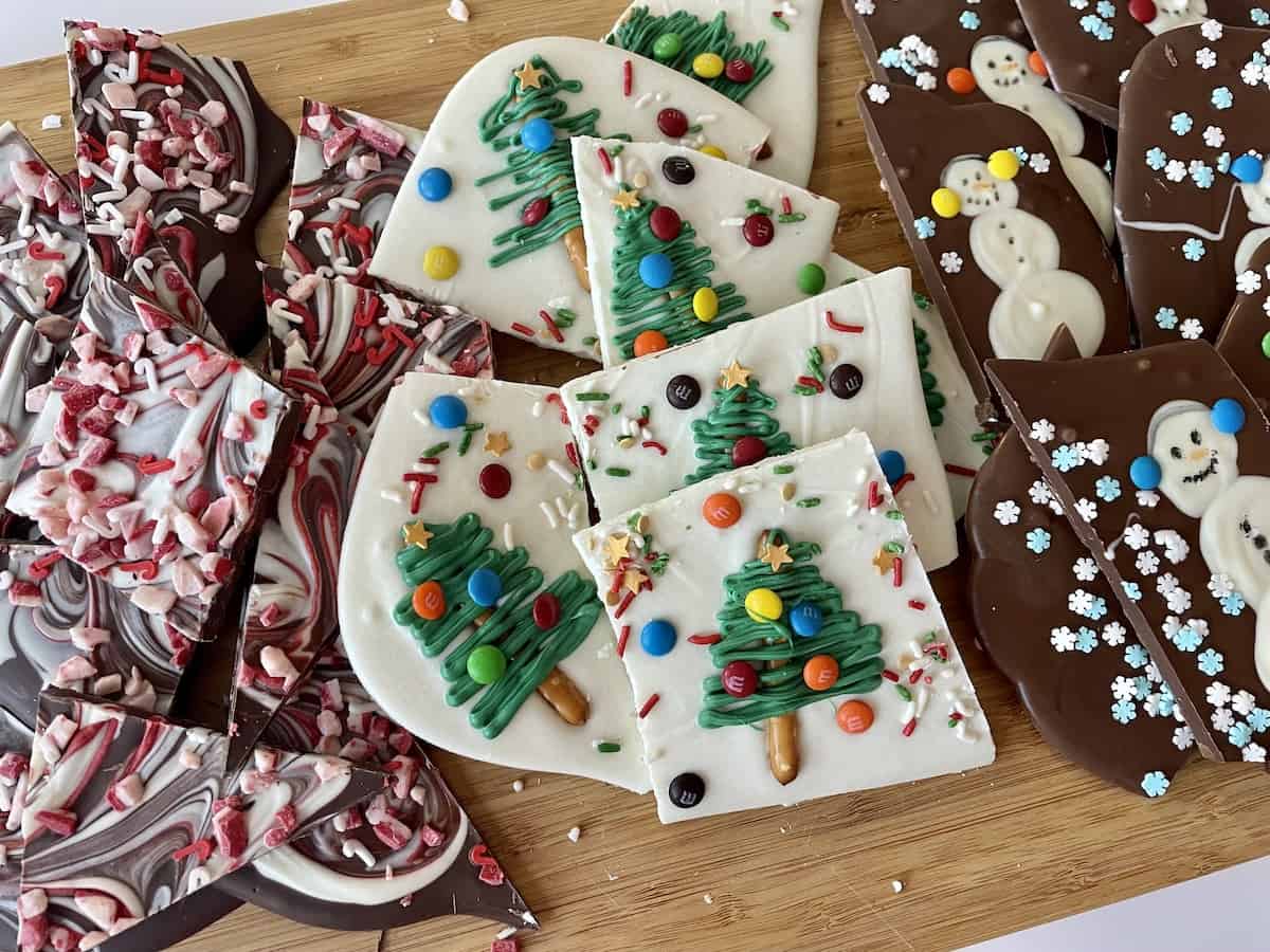 a brown cutting board with peppermint bark white chocolate christmas tree bark and milk chocolate snowmen bark