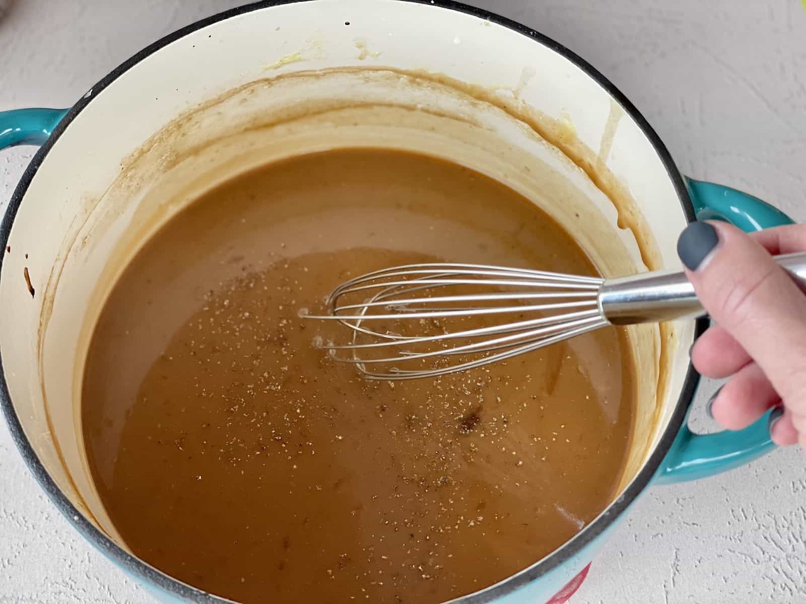 a teal enameled cast iron pot with a hand whisking gravy without drippings