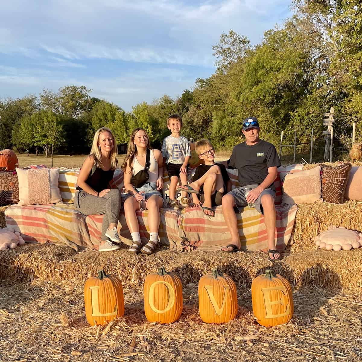 alexis leonhardt with her family sitting on hay bales with pumpkins and halloween decor