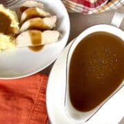 white gravy boat filled with brown gravy and a white plate of mashed potatoes and gravy with turkey