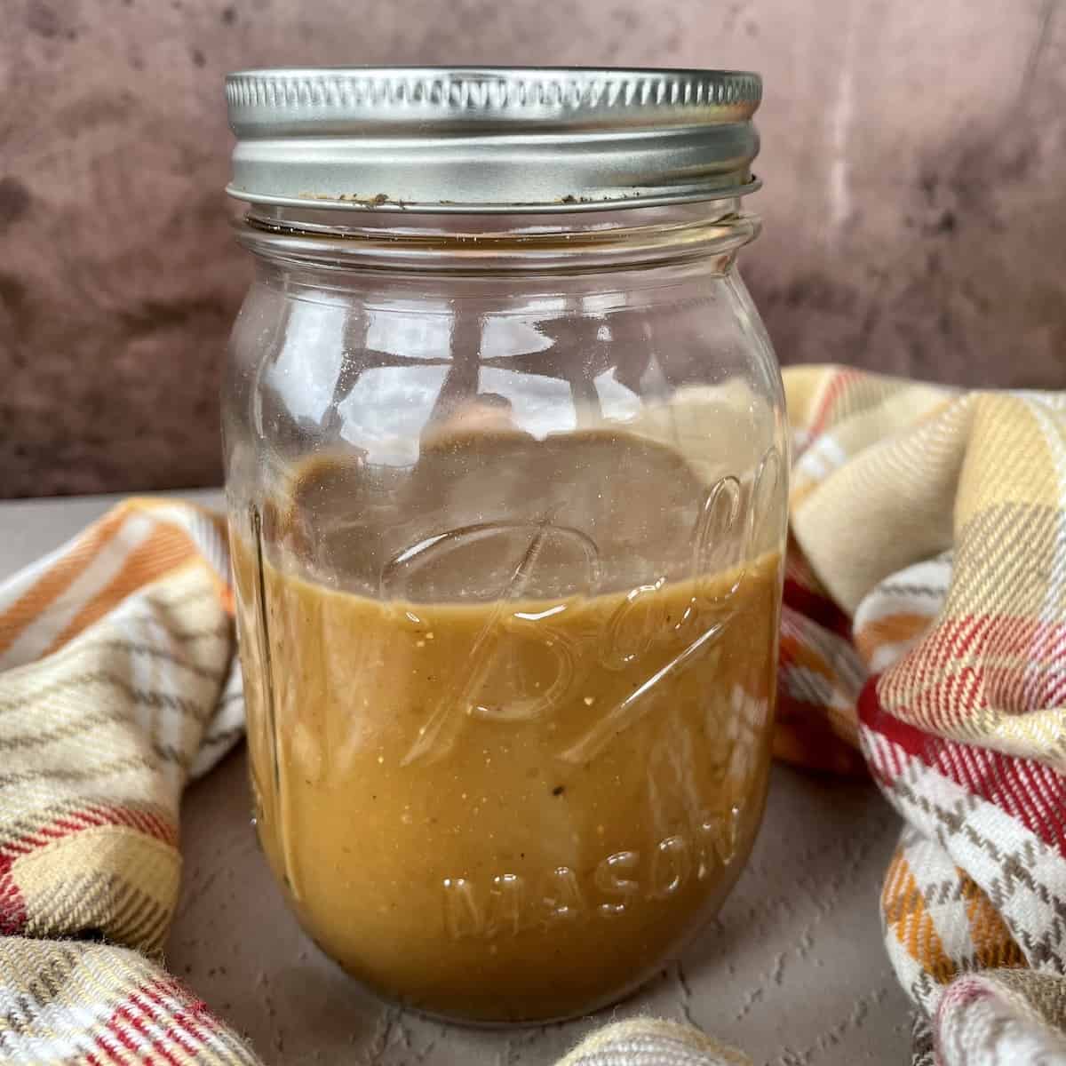 a mason jar of leftover gravy on a brown background with a orange plaid apron