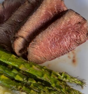 sliced filet mignon after being grilled on a traeger served on a white plate with asparagus