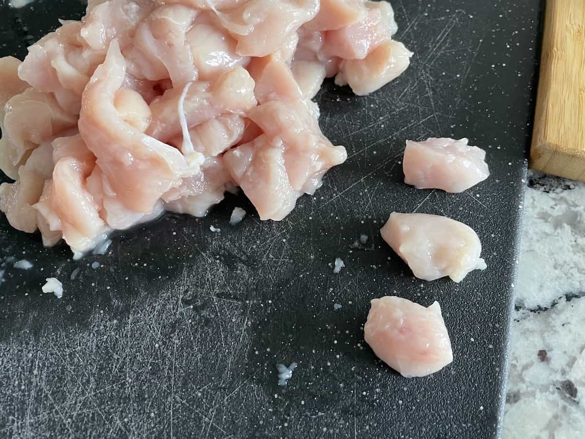 a pile of diced boneless chicken tenders cut into half inch pieces in a black cutting board