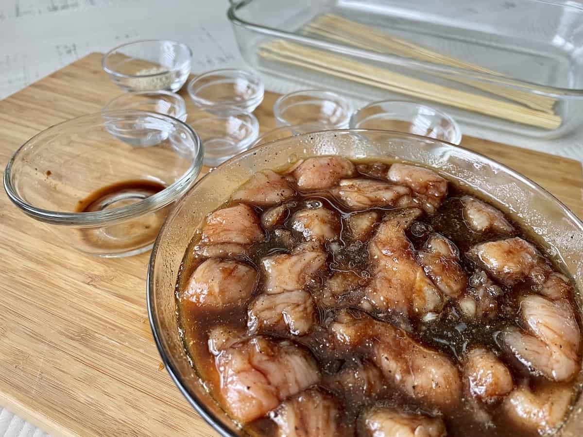 diced chicken marinating in a glass bowl with empty ingredient bowls in the background 