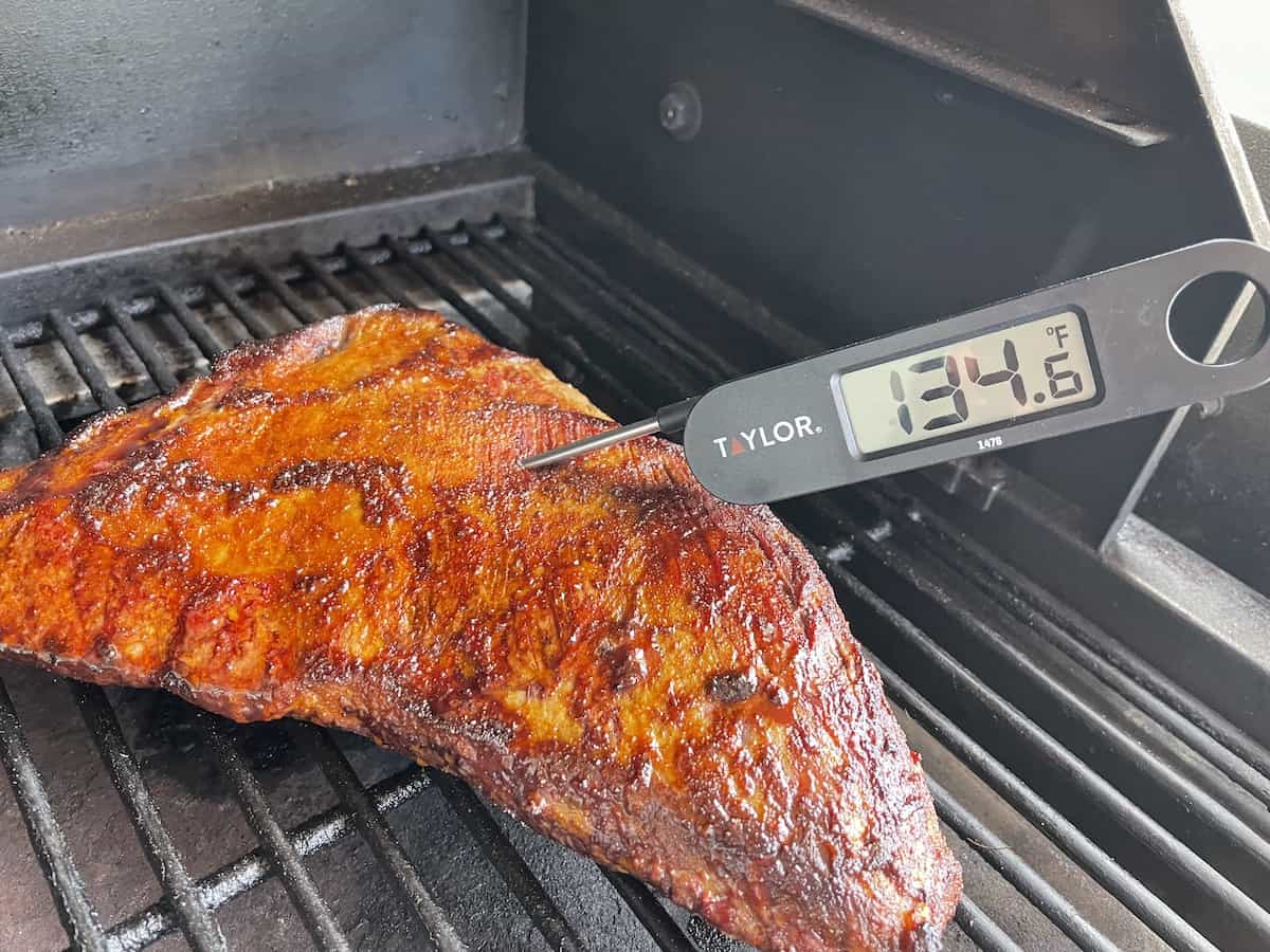 a tri tip roast cooking on a grates of the traeger grill with a digital thermometer reading a temperature of 134.6 degrees