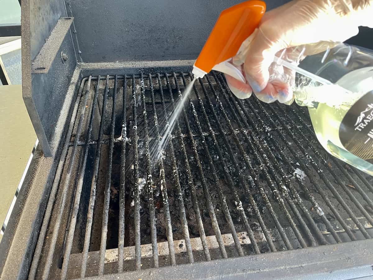 Traeger all natural spray bottle spraying cleaning solution on to dirty grill grates and messy drip pan