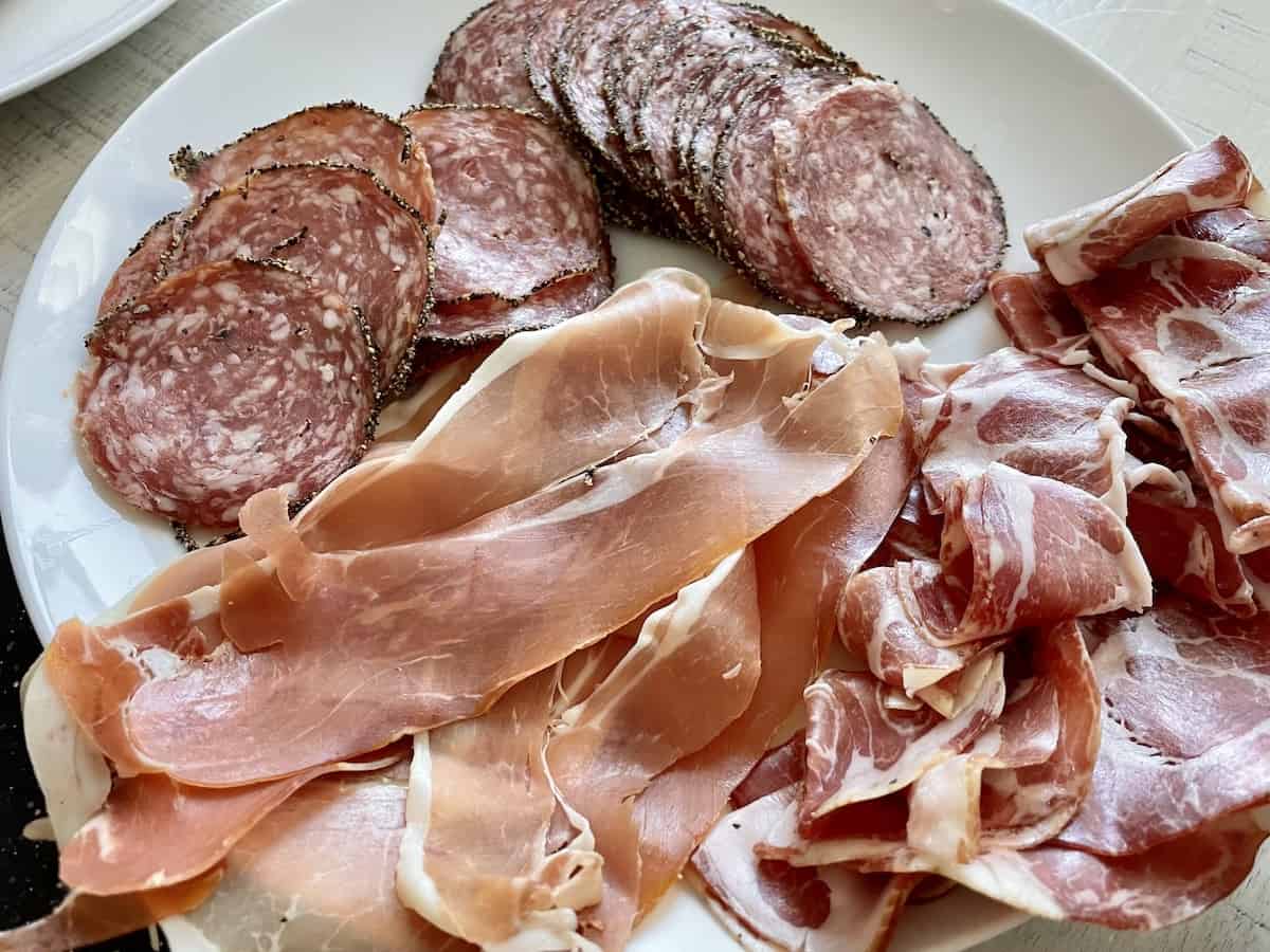 a white plate of charcuterie meats including prosciutto salami and capicola