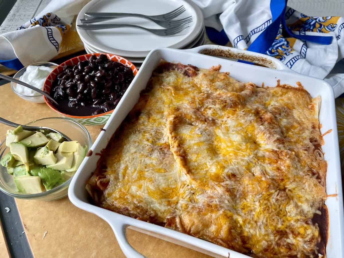 cooked beef enchilada casserole ready to serve with a bowl of black beans and diced avocado