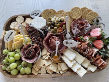 a charcuterie board filled with charcuterie meats crackers cheeses grapes strawberries marinated olives and spreads