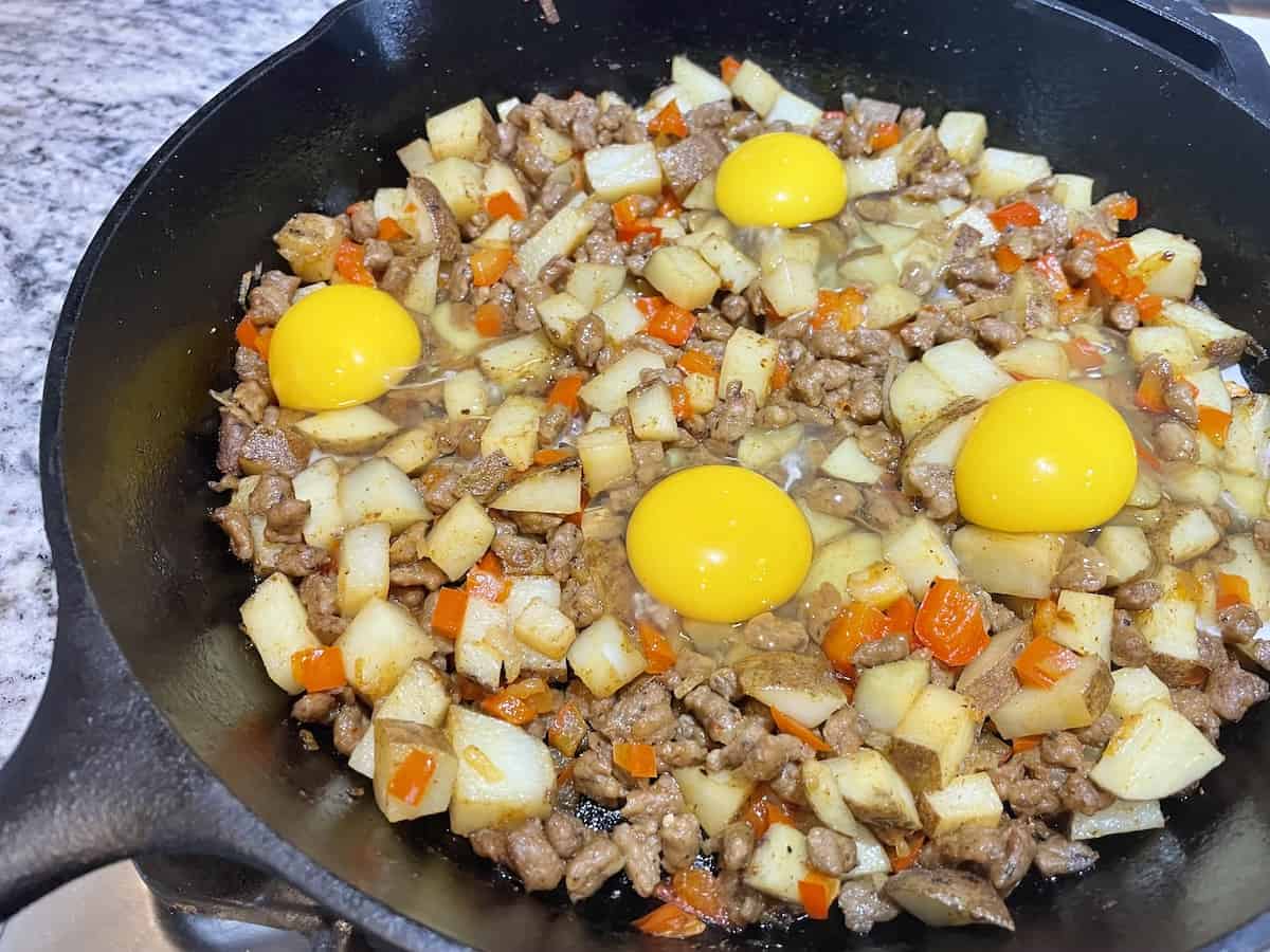 cast iron skillet with cooked potatoes and bell peppers with 4 raw eggs sitting on top 