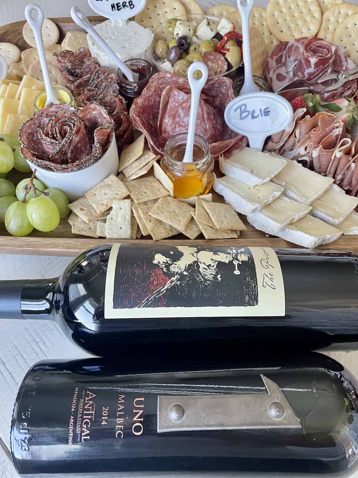 bottles of prisoner and Malbec laying on a table next to a board of meats and cheese