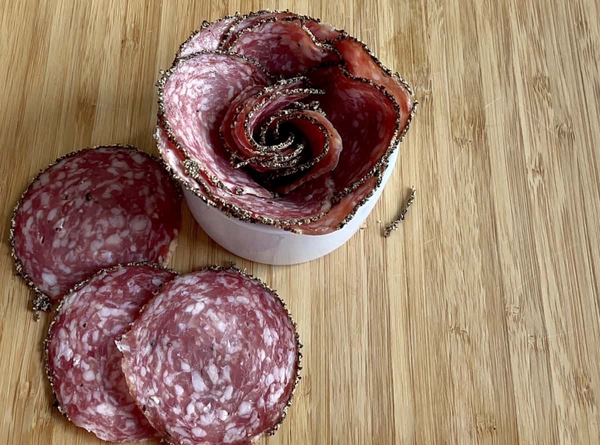 peppered salami slices overlapped in a white bowl to make a salami rose