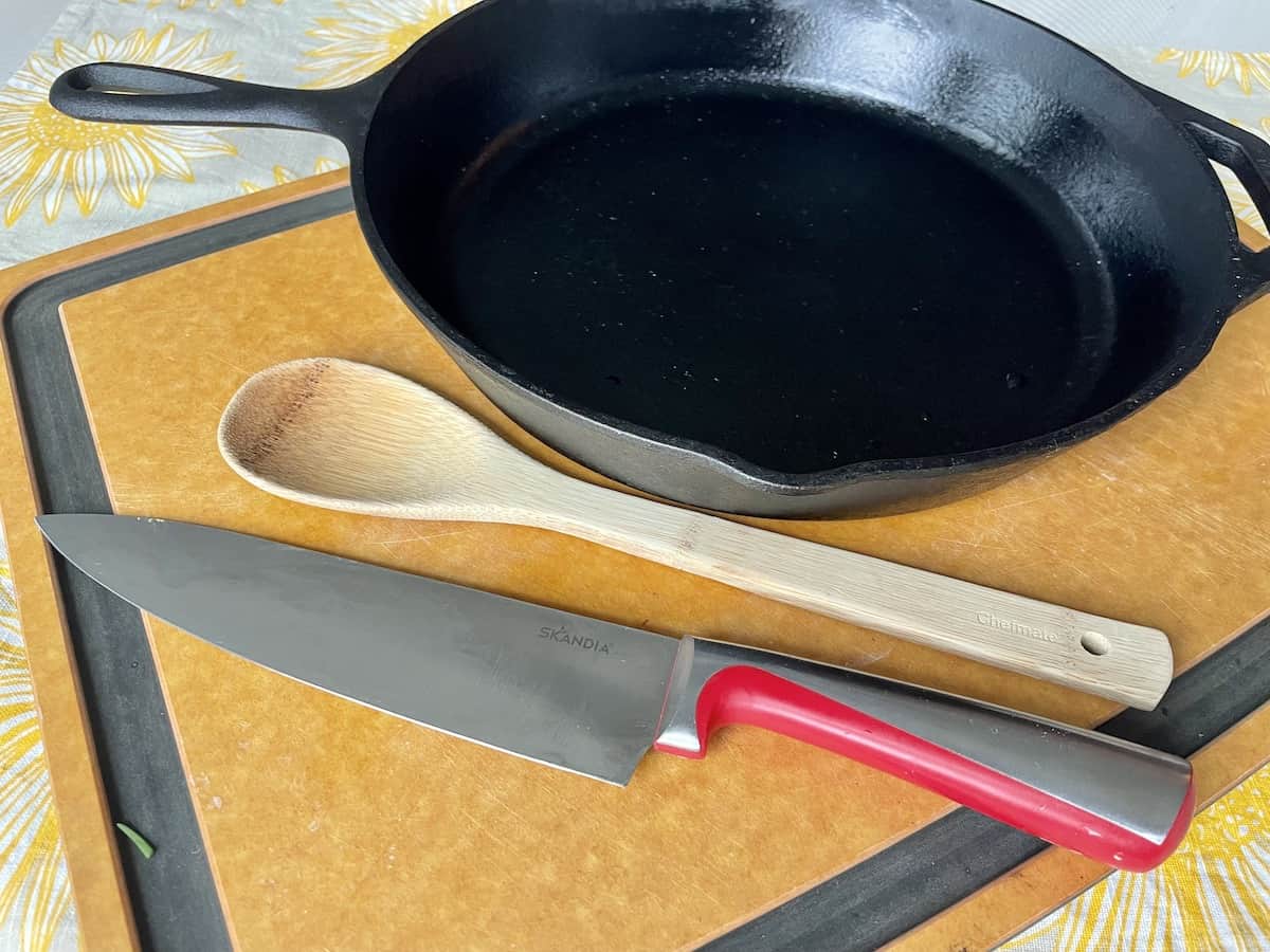 a large wood cutting board with a chefs knife wood spoon and cast iron skillet on it 