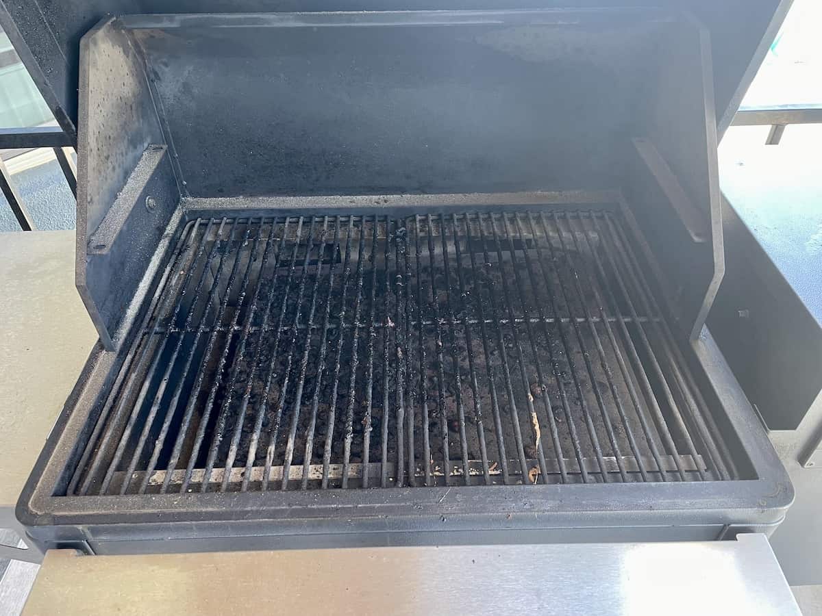 a Traeger grill with the lid open showing a very dirty drip pan with lots of grease and dirty grill grates