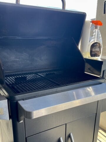 a clean Traeger grill with the lid open and a bottle of trader grill cleaner set alongside it