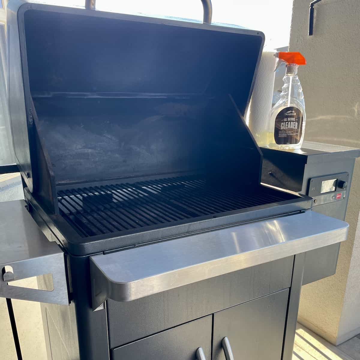 a clean Traeger grill with the lid open and a bottle of trader grill cleaner set alongside it