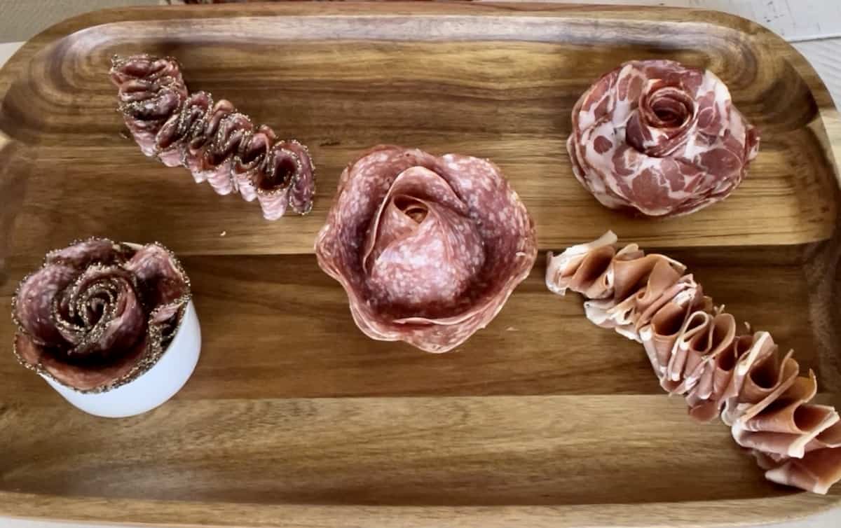 5 kinds of meat folded in various floral designs on a wood diy charcuterie board