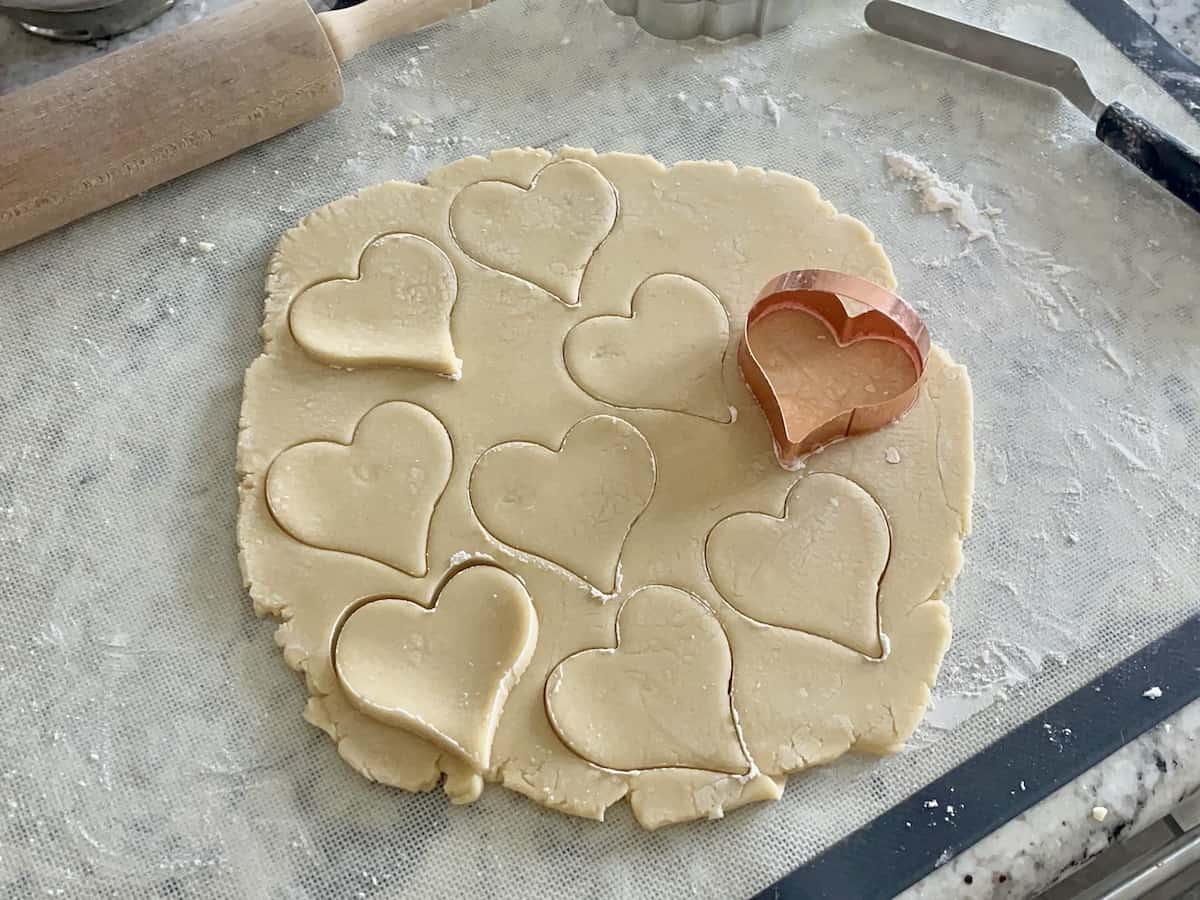 a large section of sugar cookie dough with a heart shaped cutter that has cut several cookies