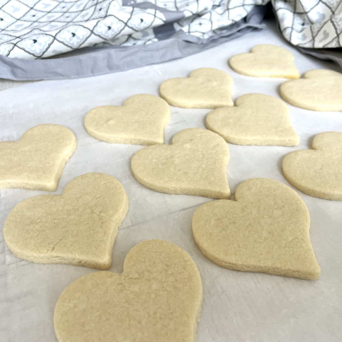 baked heart shaped sugar cookies on a white piece of parchment paper with a white and grey apron in the background