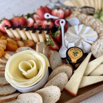 a cheese board including a provolone cheese rose cut brie cheddar triangles strawberries sliced French bread and dried apricots