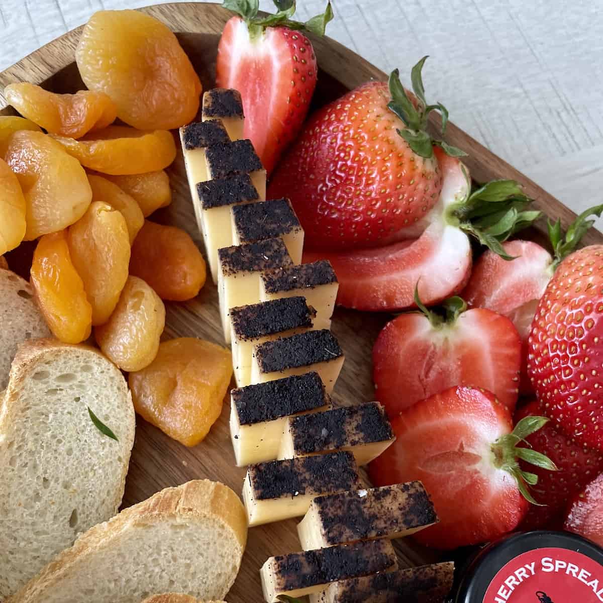 aged cheddar cheese sliced and fanned out in a tree shape with dried apricots and cut strawberries on a wood board