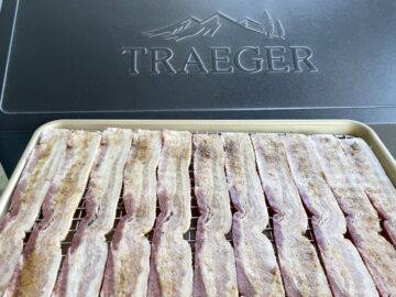 bacon brushed with brown sugar on a wire rack and sheet pan in front of a traeger grill