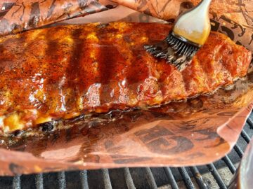 st louis ribs wrapped in paper and open to have jack daniels sauce brushed on 