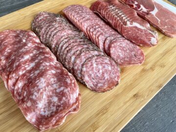 large salami circles black pepper salami Genoa salami copper and prosciutto lined on a wood cutting board