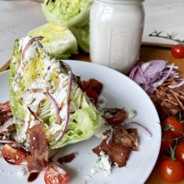 a wedge salad served on a white plate with salad ingredients in the background 