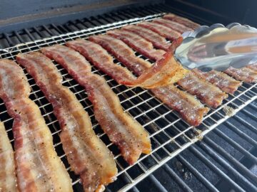 bacon jerky being flipped with tongs in the traeger grill