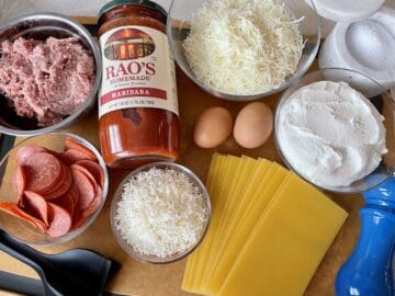 a wood cutting board with all of the raw ingredients for making pizzagna