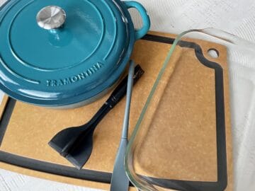 large teal enabled cast iron pot on a wood cutting board with a 9x13 glass baking dish meat masher and small rubber spatula