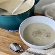 teal dutch oven with a ladle and potato soup with a white bowl soup next to it