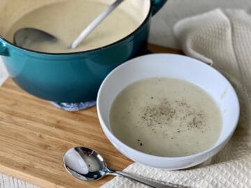 teal dutch oven with a ladle and potato soup with a white bowl soup next to it