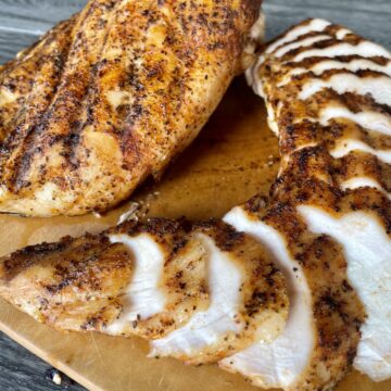 smoked chicken breast on a wood cutting board one whole breast and one sliced