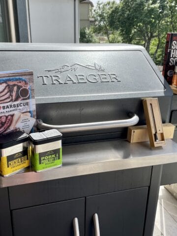 Traeger smoker with Traeger rubs a wood cutting board meater plus thermometer and cookbooks on top