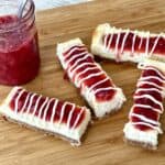 4 philadelphia cheesecake bars on a wood cutting board with a jar of strawberry sauce