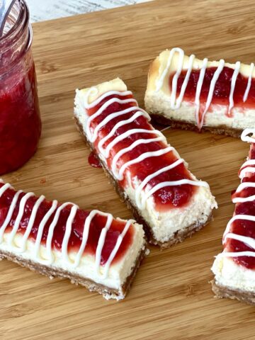 4 philadelphia cheesecake bars on a wood cutting board with a jar of strawberry sauce