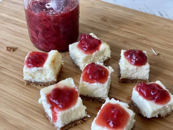 mini cheesecake squares on wood cutting board with strawberry sauce 