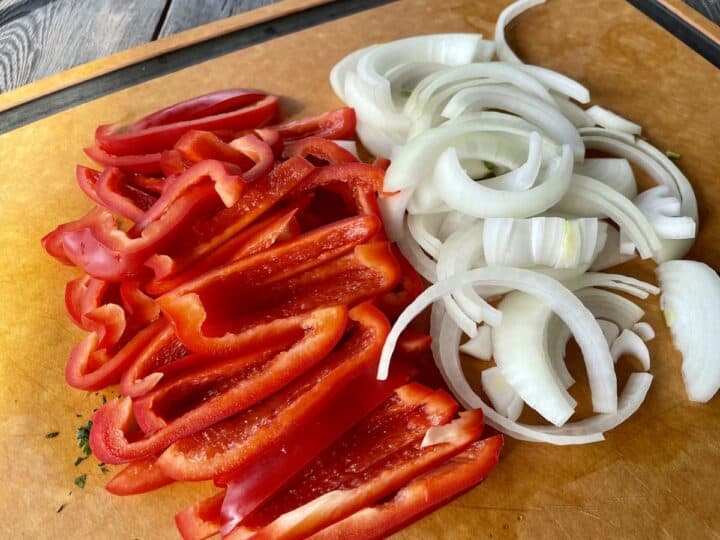 sliced red bed pepper and yellow onion on a wood cutting board