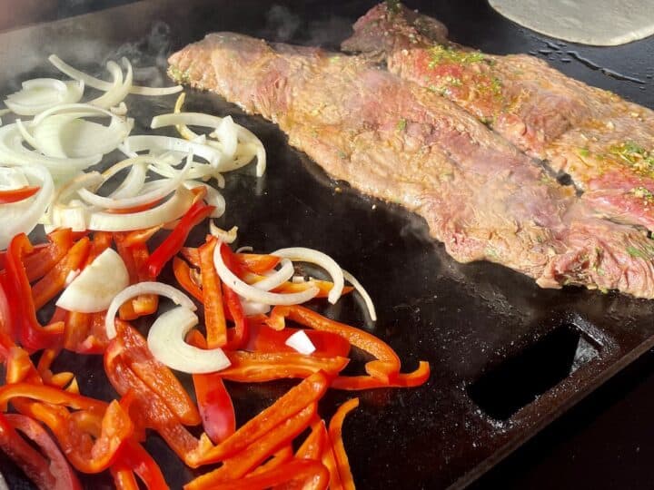 red bell pepper sliced onion and marinated skirt steak cooking on a Traeger flatrock