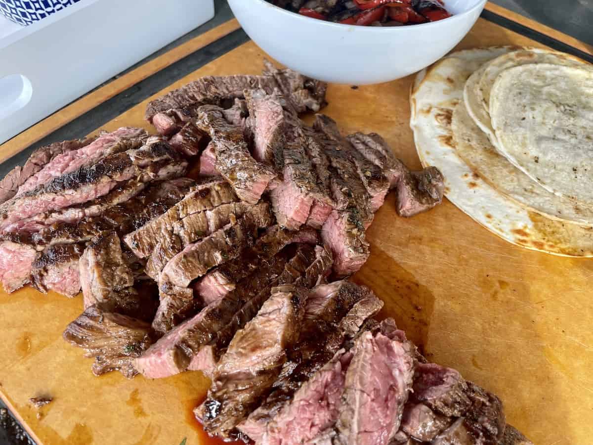 sliced skirt steak on a wood cutting board with warm tortillas