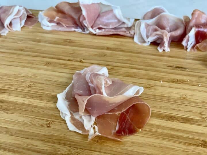 gently piled prosciutto on a wood cutting board