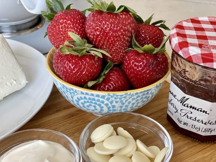 blue bowl of fresh strawberries next to strawberry jam and white chocolate